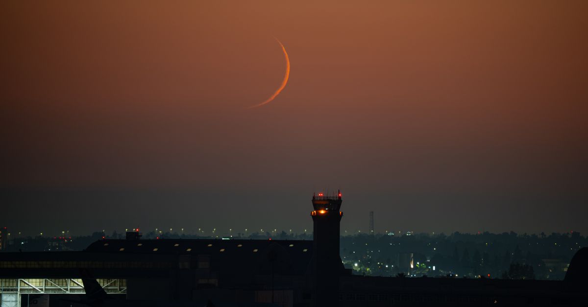 The main subject of the photograph is a crescent moon over an airport, with a control tower and runway in the foreground.