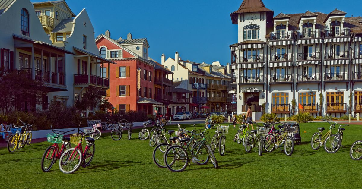 A group of bicycles parked on a lawn in front of buildings.