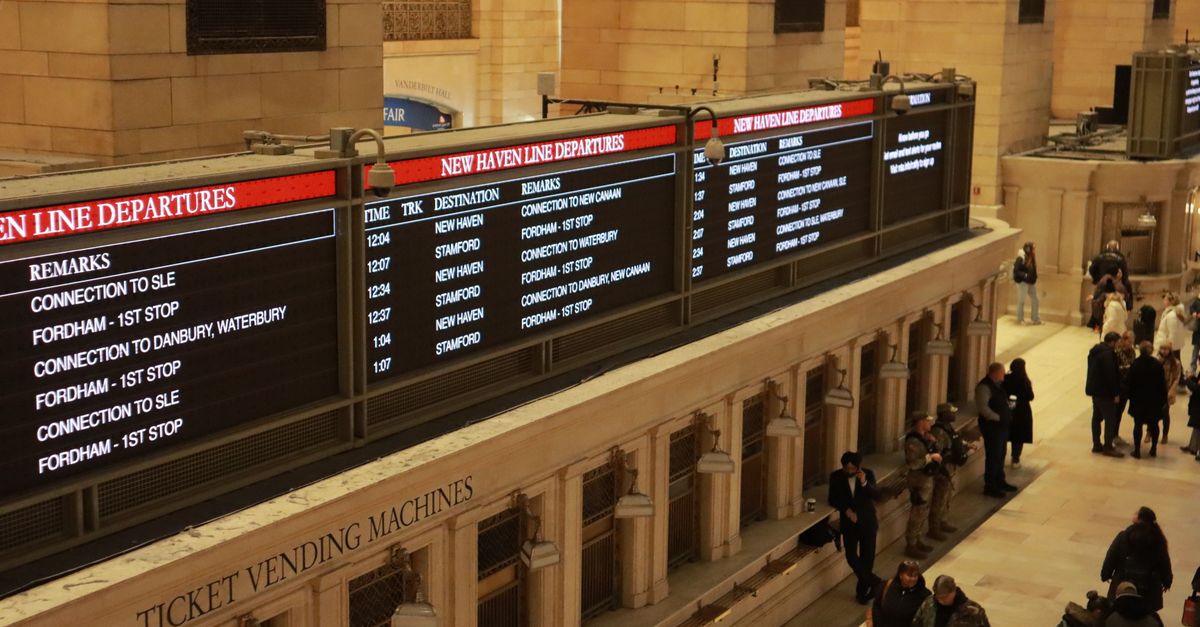 A train station platform with a large digital departures board displaying information about trains and their destinations.