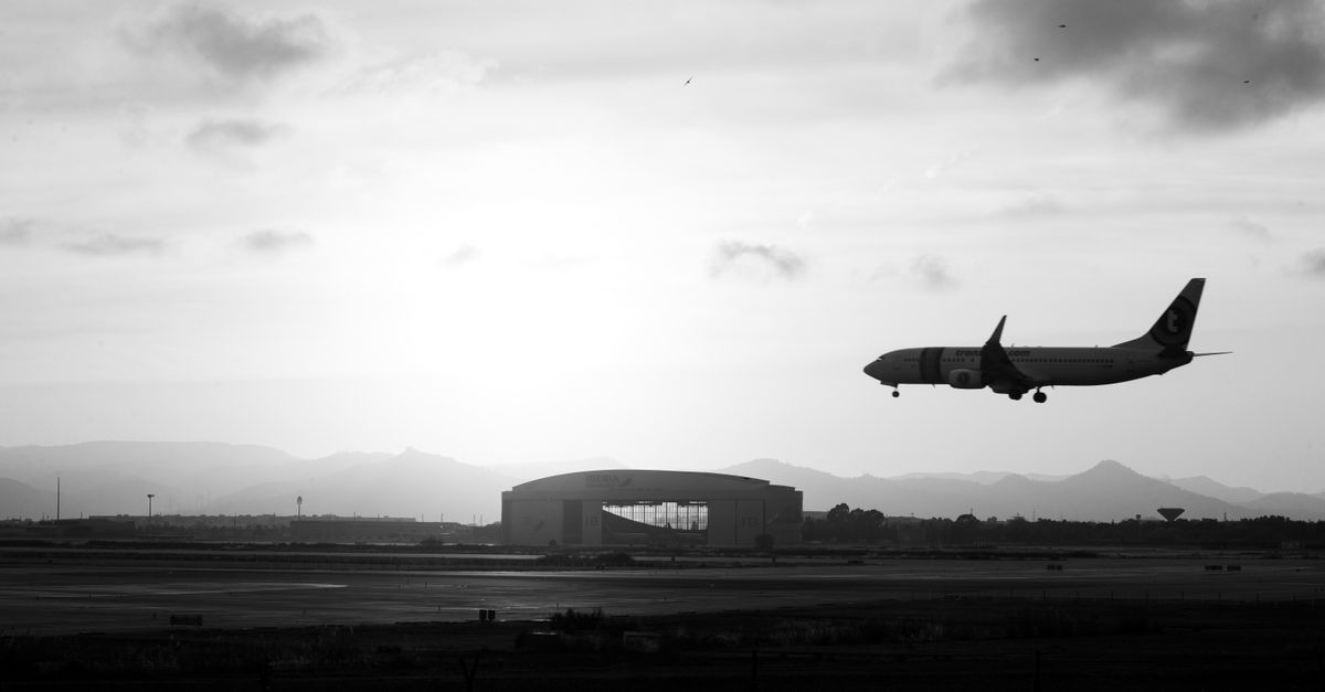 A silhouette of an airplane landing against a dramatic sunset, with mountains in the background.