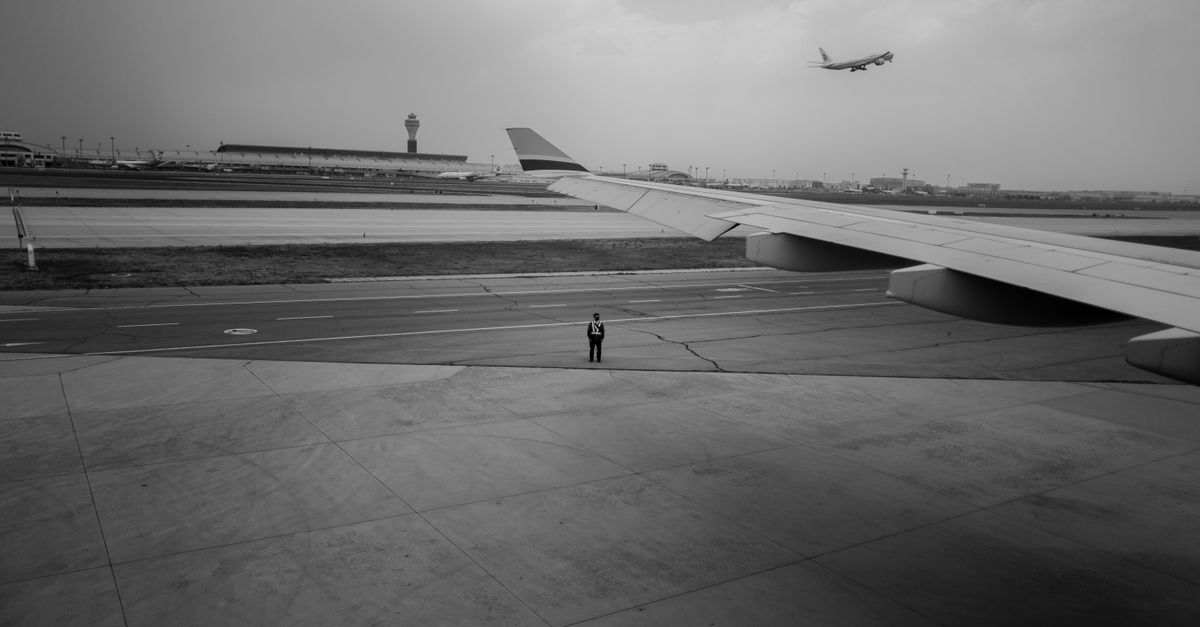 Dramatic black and white view of an airport runway with airplane wing and control tower.