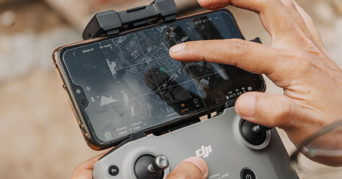 Hands manipulating DJI drone controller with smartphone, showcasing navigation technology.