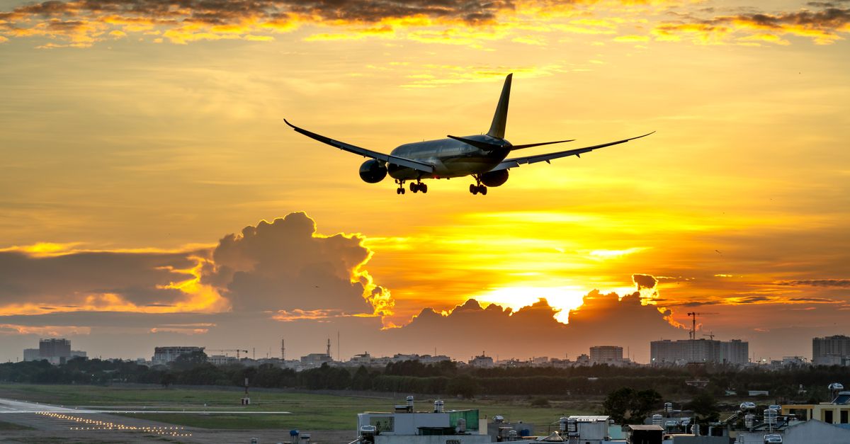 A dramatic image of an airplane landing against a vibrant sunset over a city skyline.