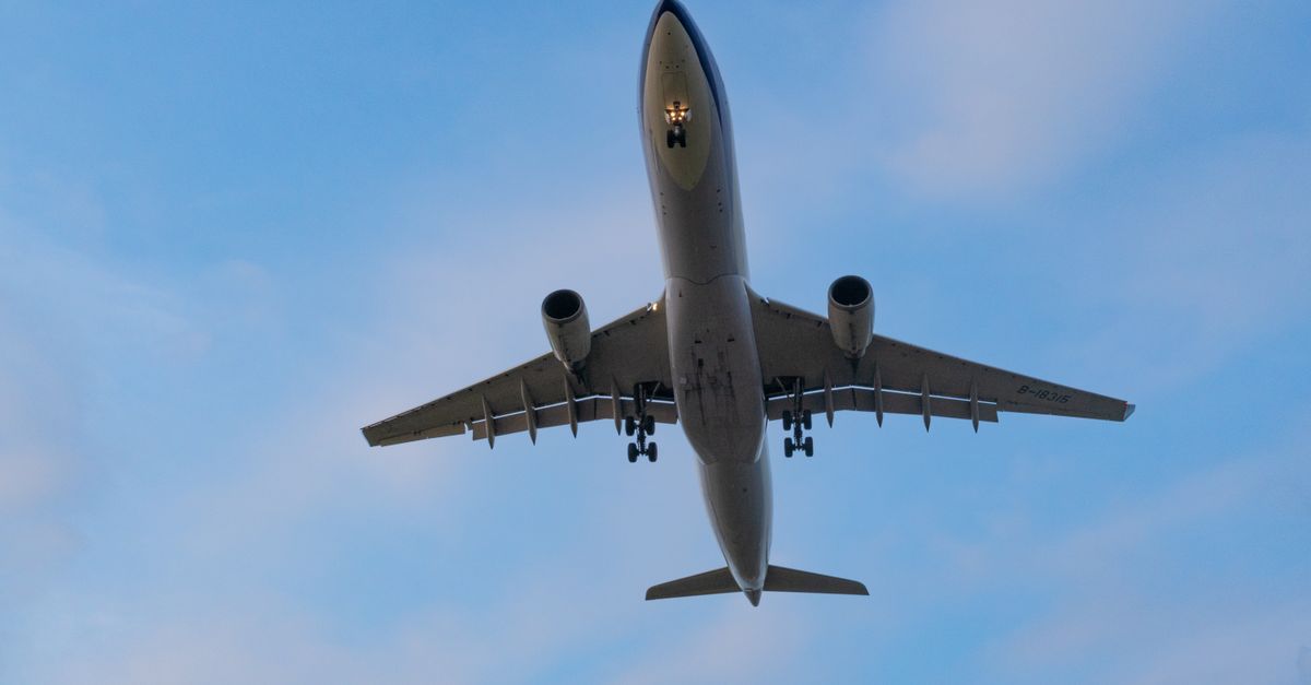 A dramatic shot of an airplane flying overhead during the day against a bright blue sky.