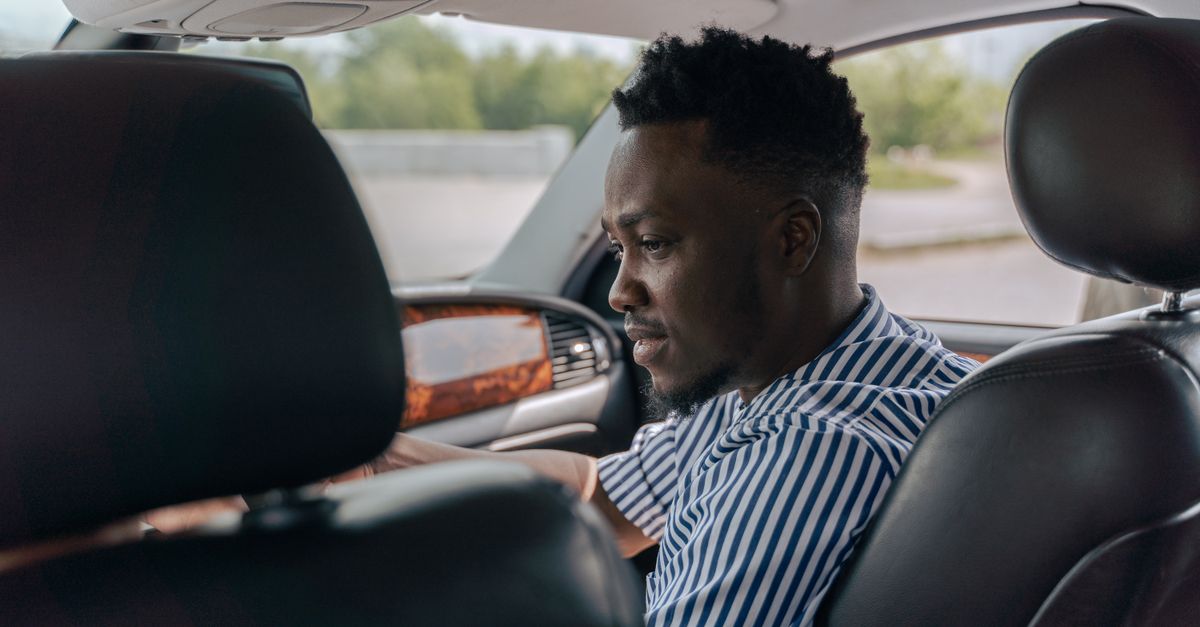 A man seated inside a car, looking down at his phone