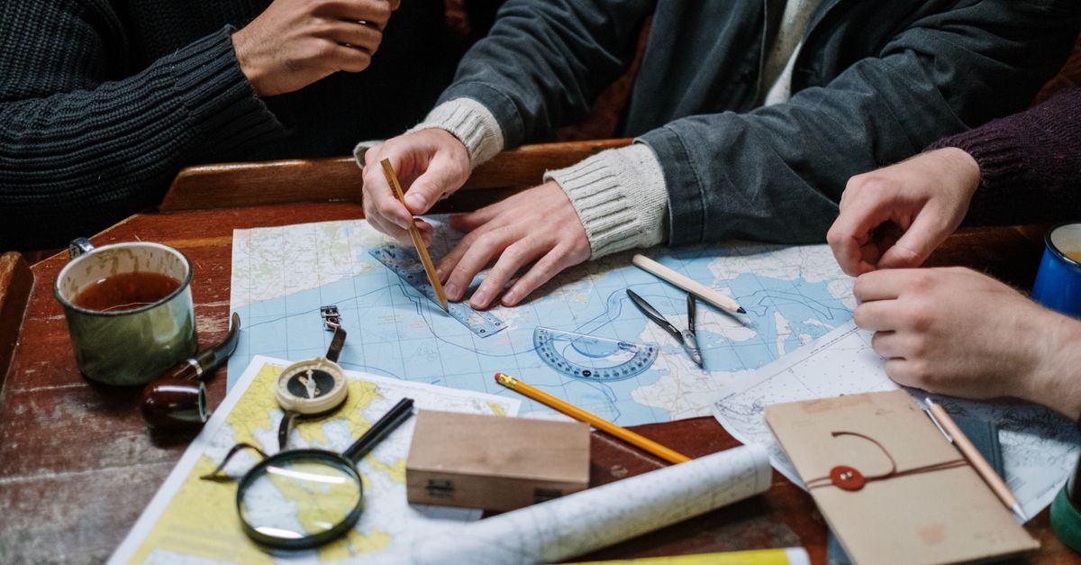 Adults planning a nautical journey using maps, compass, and tools indoors.