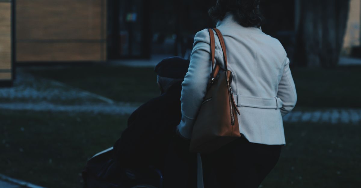 A woman assists a person in a wheelchair outdoors, demonstrating care.