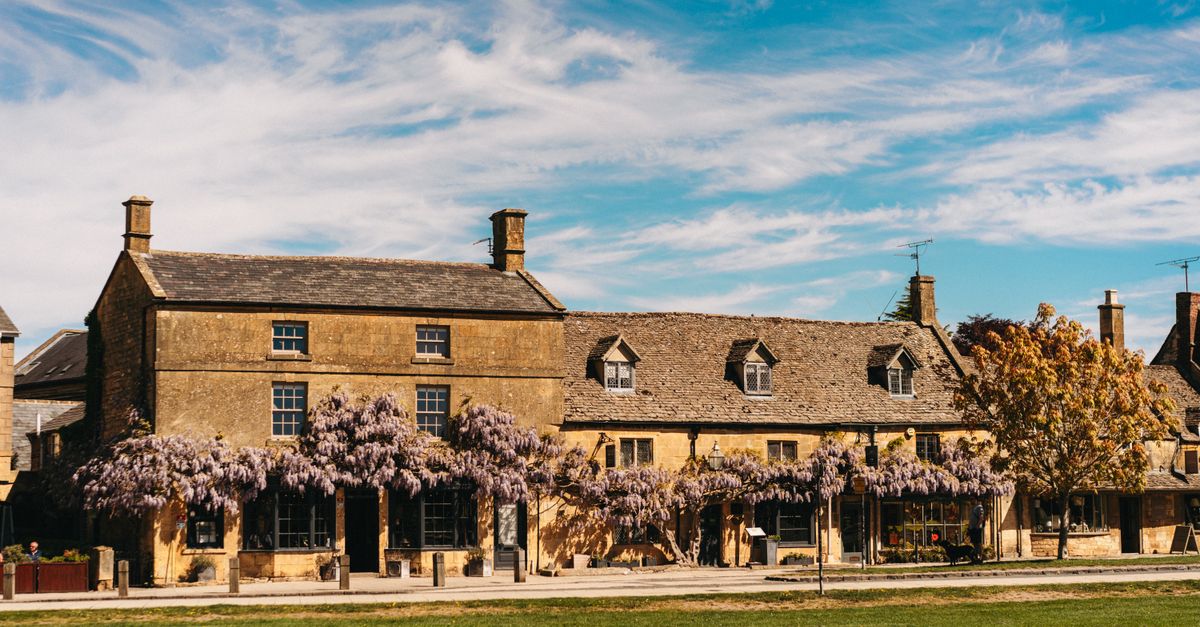 Picturesque historic building in the Cotswolds adorned with vibrant wisteria under a blue sky.