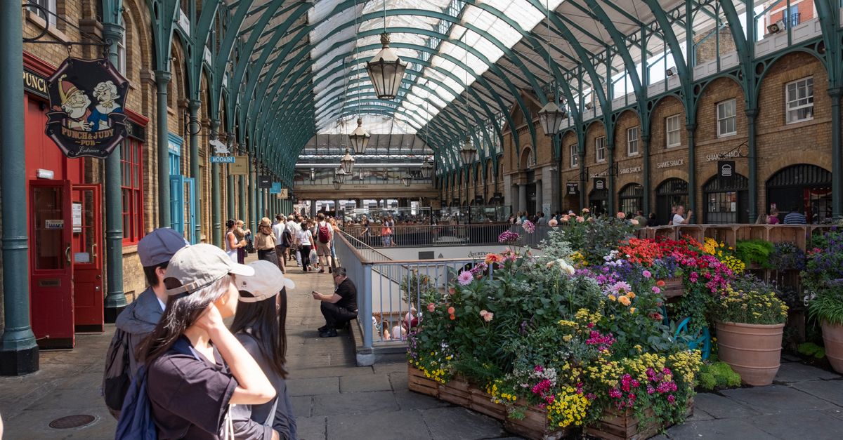 Vibrant flowers in London's iconic Covent Garden Market, busy with tourists and locals enjoying a sunny day.