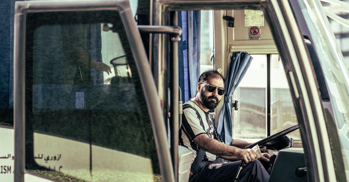 Confident bus driver in sunglasses sits behind the wheel, ready for travel.