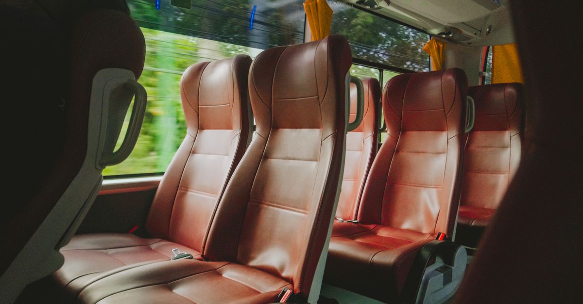 Row of empty coach seats viewed from inside, with countryside blurred through the window.