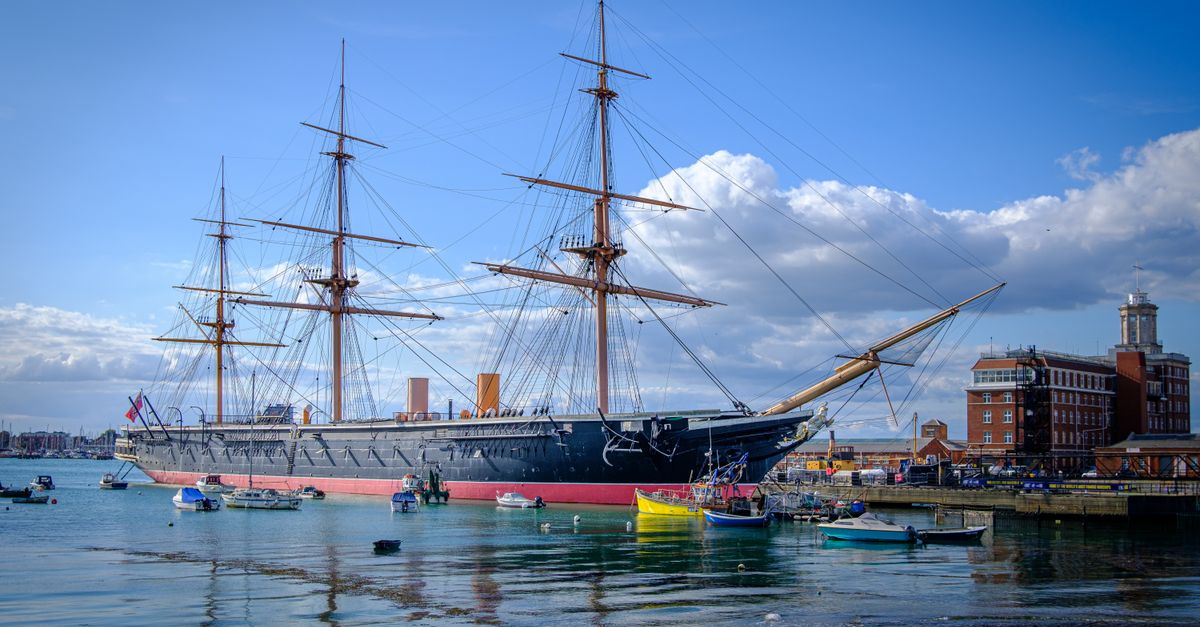 HMS Warrior historic ship moored in Portsmouth Harbour with small boats around it.