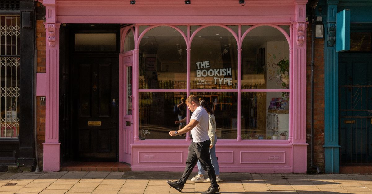 Vibrant pink bookstore facade on a sunny street in Leeds, UK, with people walking by.