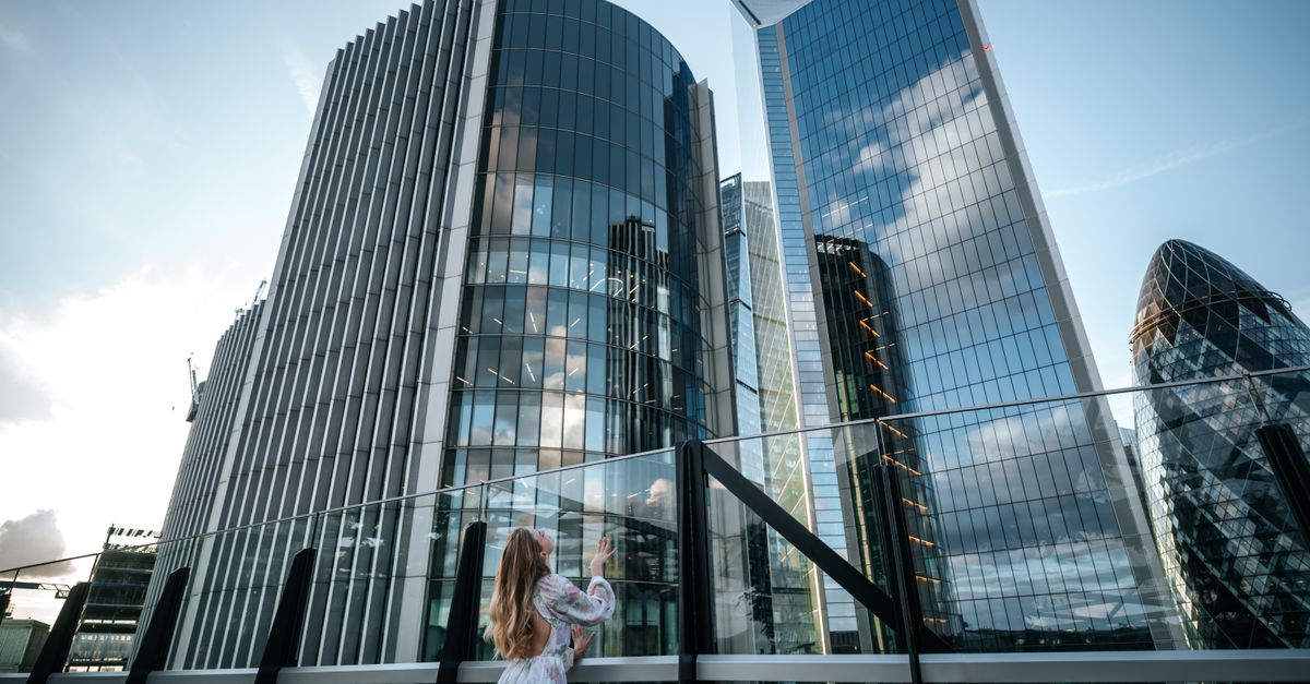 A young woman gazes at London's iconic skyscrapers in a modern urban setting.