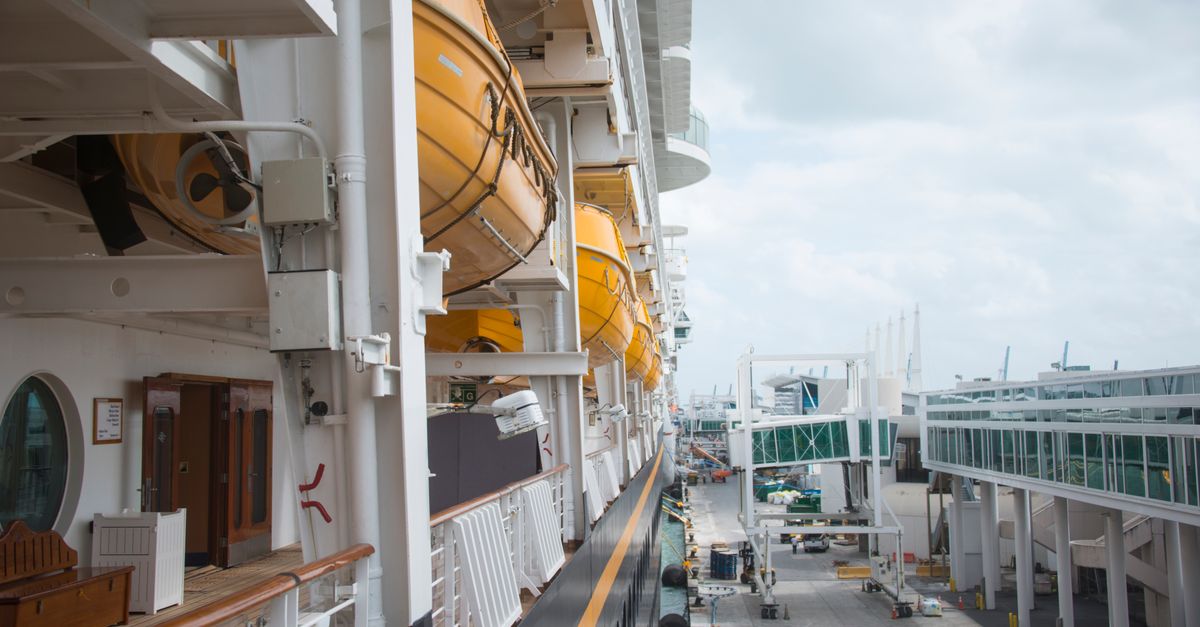 View along a cruise ship's deck and lifeboats moored beside a modern cruise terminal.