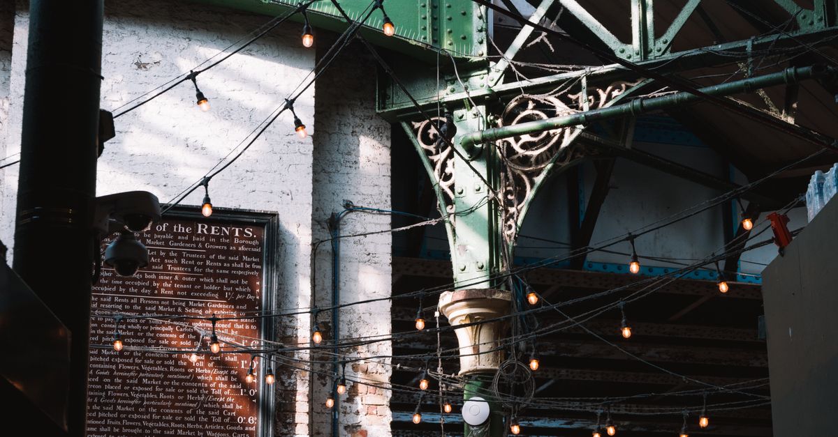 Intricate ironwork beams and string lights create a vintage urban atmosphere in London's historic district.