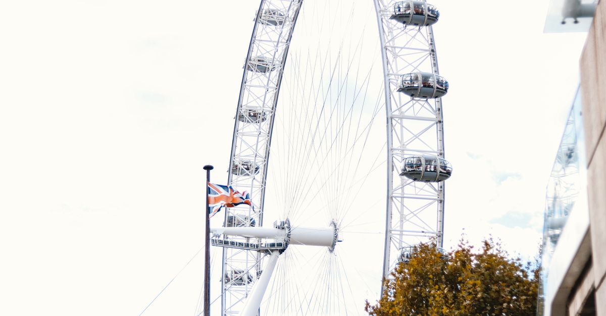 Low angle view of the iconic London Eye with autumn trees and Union Jack flag.