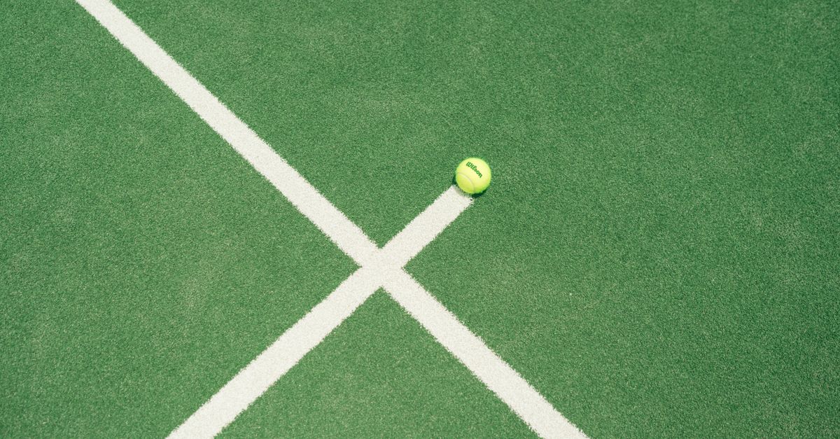 A bright green tennis ball on a green tennis court with white lines in Miami, FL.