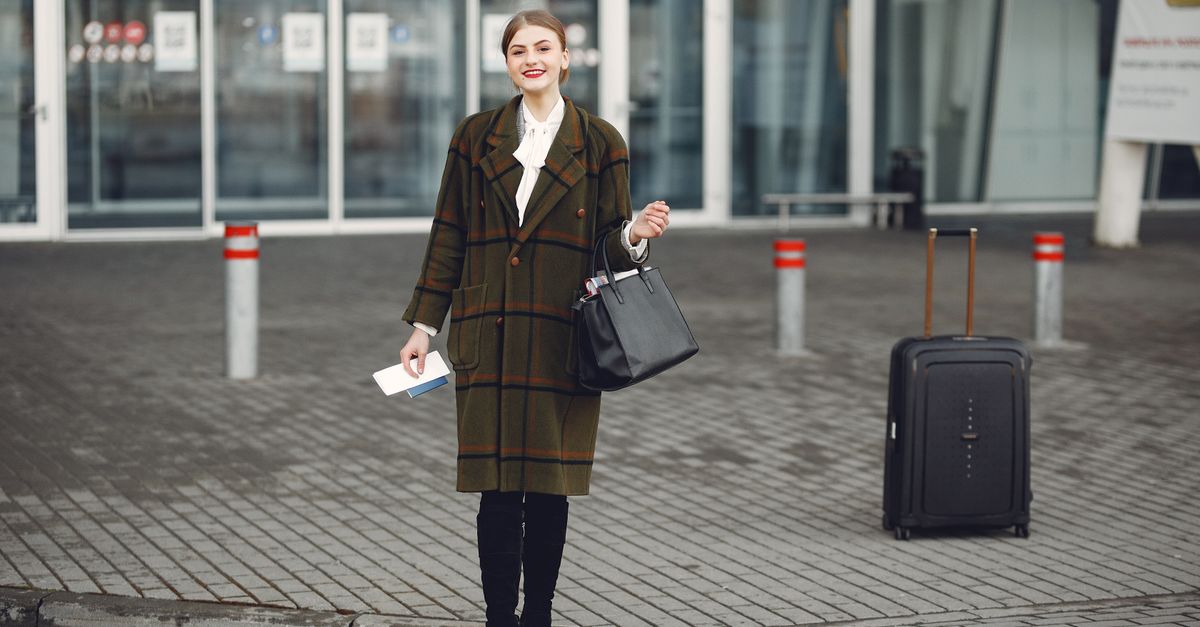 Traveller with a passport and rolling suitcase outside a glass-fronted terminal entrance.